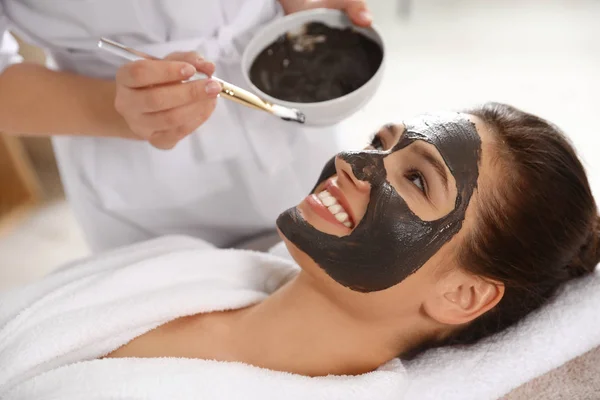 Kozmetikus alkalmazó fekete maszk-ra asszony arca Spa szalon — Stock Fotó