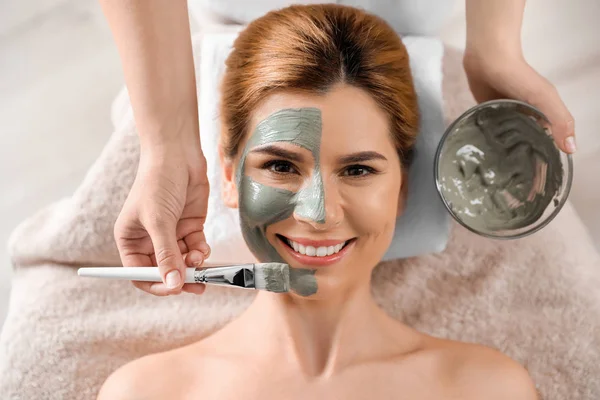 Kosmetologis menerapkan topeng ke wajah wanita di spa salon, pandangan atas — Stok Foto