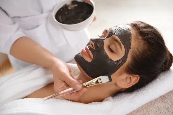 Kosmetologis menerapkan topeng hitam ke wajah wanita di spa salon — Stok Foto