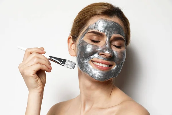 Beautiful woman applying mask onto face against light background — Stock Photo, Image