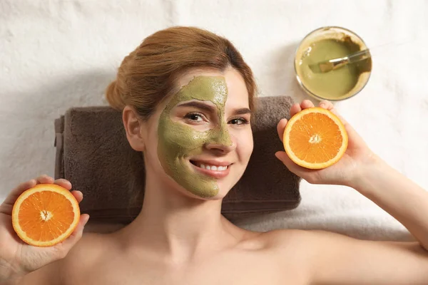 Wanita cantik dengan topeng di wajah dan memotong orange relaxing di spa salon, top view — Stok Foto
