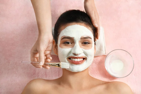 Kosmetologis menerapkan topeng putih ke wajah wanita di spa salon, pandangan atas — Stok Foto