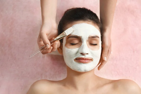 Cosmetologue appliquer un masque blanc sur le visage de la femme dans le salon de spa, vue de dessus — Photo