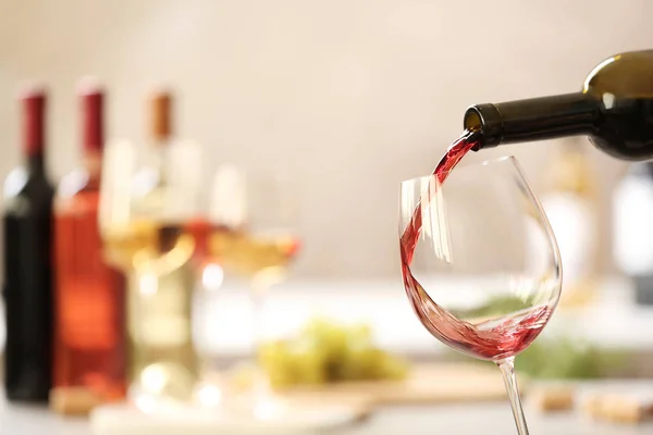 Verter el vino tinto de la botella en un vaso sobre un fondo borroso. Espacio para texto — Foto de Stock
