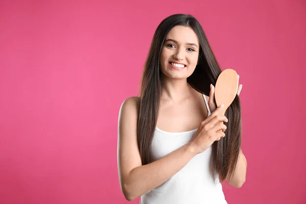 Beautiful smiling young woman with hair brush on color background — Stock Photo, Image