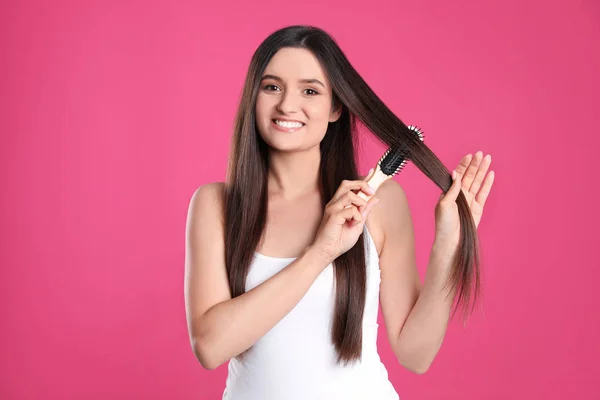 Bela jovem sorridente com escova de cabelo no fundo de cor — Fotografia de Stock