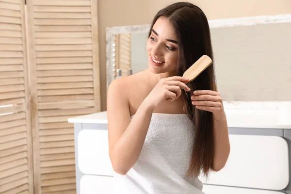 Beautiful smiling young woman with hair brush in bathroom — Stock Photo, Image