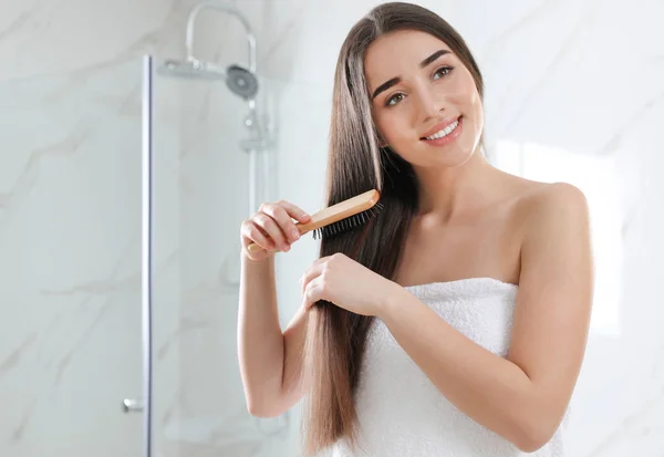 Beautiful young woman with hair brush in bathroom — Stock Photo, Image