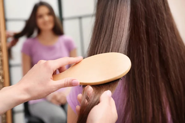 Mujer peinando el pelo de un amigo con un cepillo de cojín en el interior, primer plano — Foto de Stock