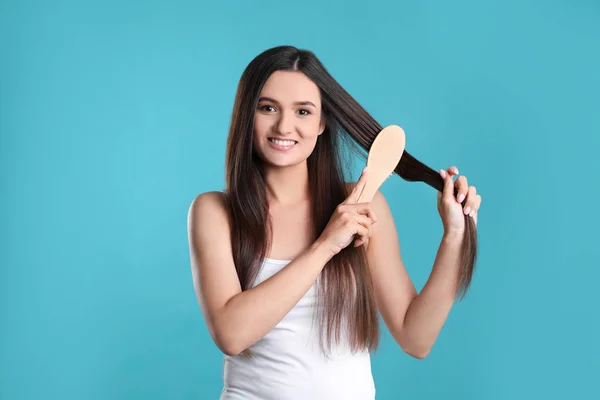 Bella sorridente giovane donna con spazzola per capelli su sfondo di colore — Foto Stock