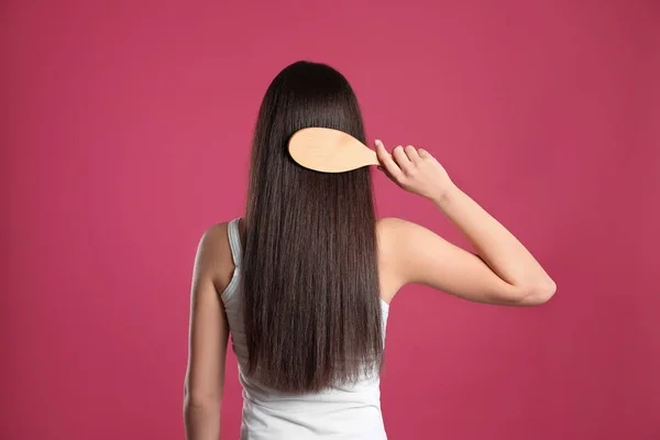 Back view of young woman with hair brush on color background — Stock Photo, Image