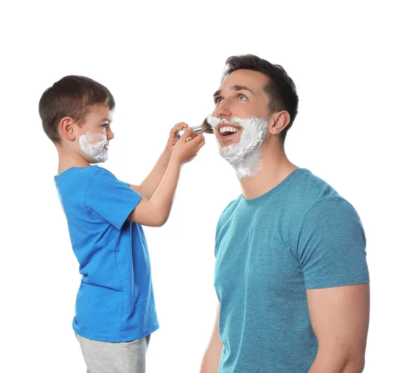 Pequeno filho aplicando espuma de barbear no rosto do pai contra o fundo branco — Fotografia de Stock