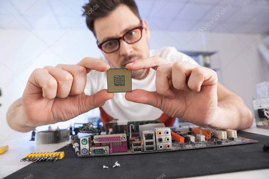 Male technician repairing motherboard at table indoors