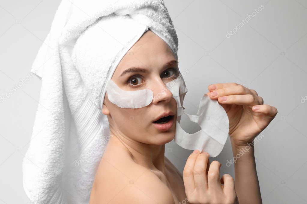 Emotional woman with cotton face and eye masks against light background