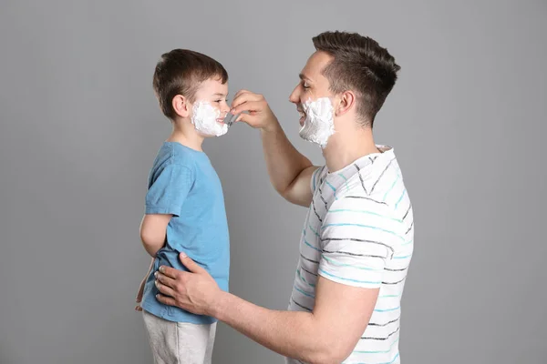 Papa pretenderen te scheren zijn kleine zoon op kleur achtergrond — Stockfoto
