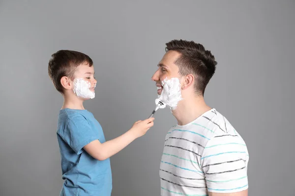 Pequeño hijo afeitando a su padre sobre fondo de color — Foto de Stock