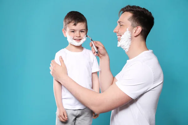 Tata udaje mu się golić jego małego syna na kolorowym tle — Zdjęcie stockowe