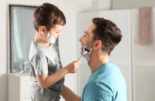 Kleine zoon het scheren van zijn vader in de badkamer — Stockfoto