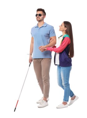 Young woman helping blind person with long cane on white background