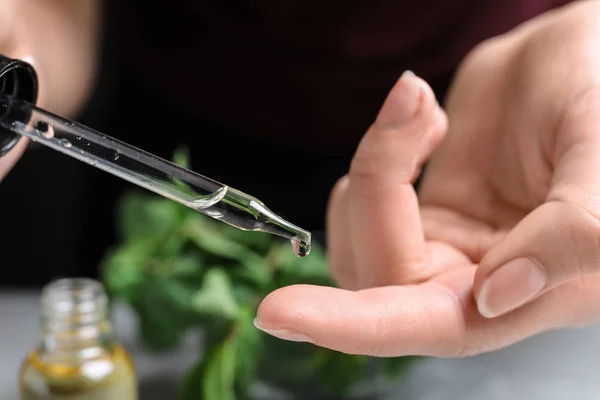 Donna che gocciola olio essenziale sul dito su sfondo sfocato, primo piano — Foto Stock