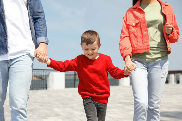 Happy child holding hands with his parents outdoors. Family weekend