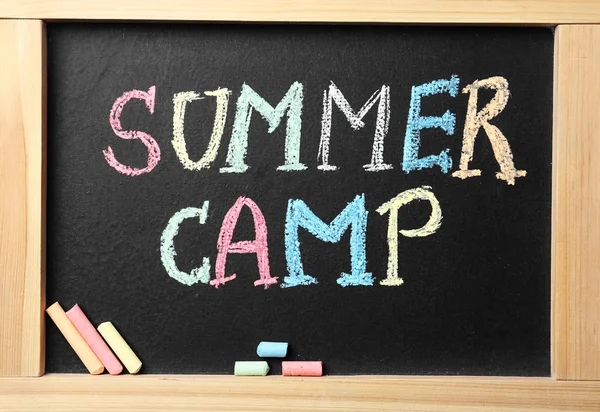 Small blackboard with text SUMMER CAMP and chalk sticks, flat lay