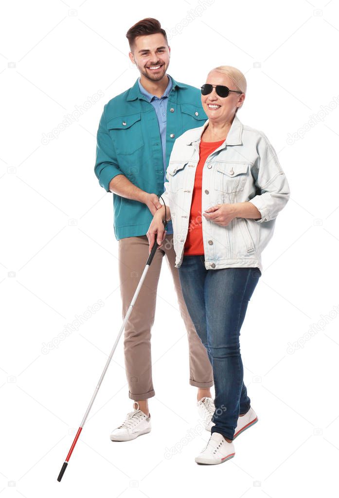 Young man helping blind person with long cane on white background
