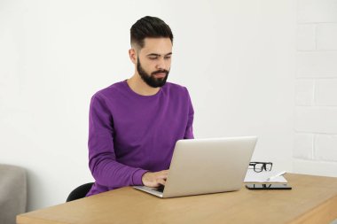 Yakışıklı genç adam ev ofisinde masada dizüstü bilgisayar ile çalışıyor