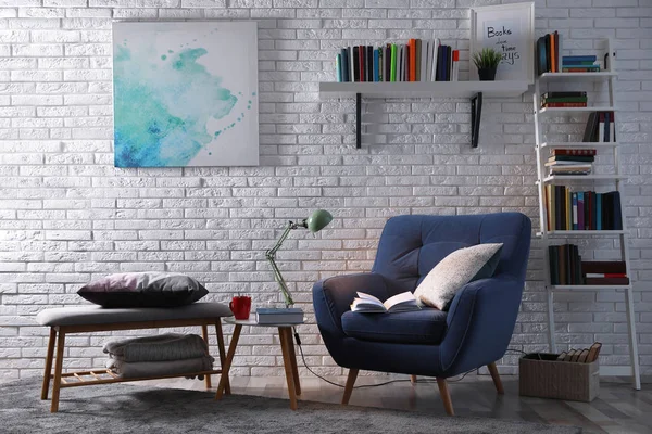 Intérieur de la chambre avec fauteuil confortable et différents livres près du mur de briques — Photo