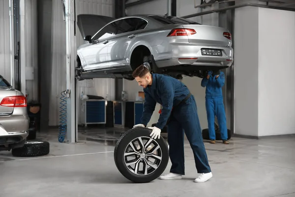 Técnico com roda de carro na oficina de reparação de automóveis — Fotografia de Stock