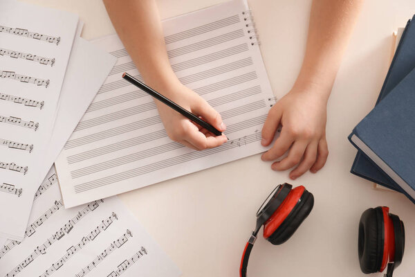 Child writing music notes at table, top view