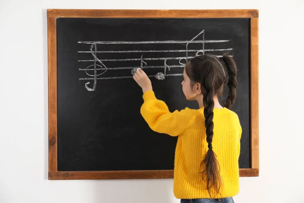 Menina escrevendo notas de música no quadro negro em sala de aula — Fotografia de Stock