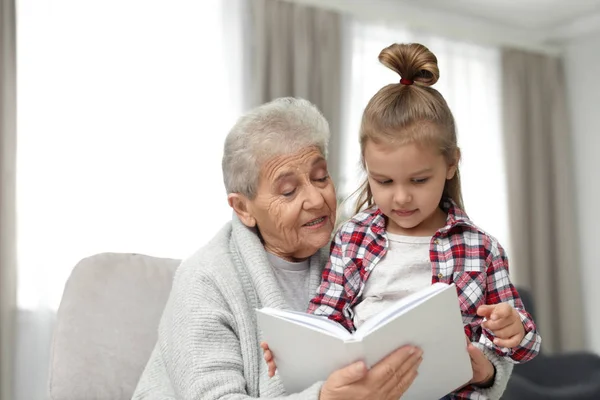 Menina bonito e sua avó ler livro em casa — Fotografia de Stock