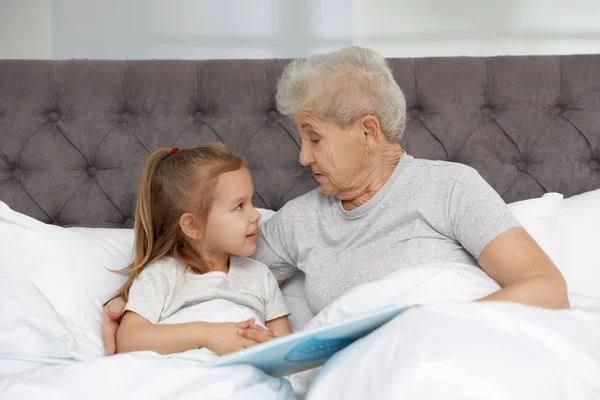 Fille mignonne et sa grand-mère lecture livre sur le lit à la maison — Photo