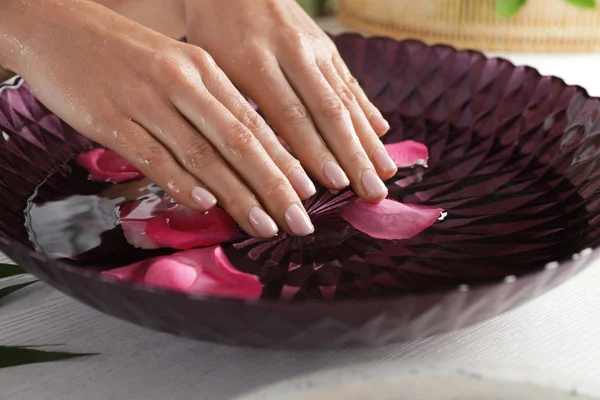 Woman soaking her hands in bowl with water and petals on table, closeup. Spa treatment — Stockfoto