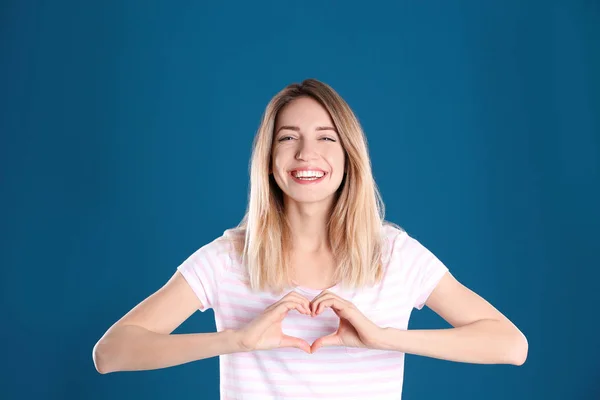 Portret van mooie vrouw maken hart met haar handen op kleur achtergrond — Stockfoto