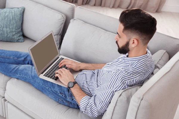 Schöner junger Mann arbeitet mit Laptop auf Sofa zu Hause — Stockfoto