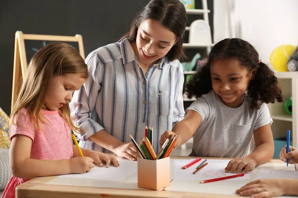 Aranyos kis gyermekek iskolai tanár rajzot az asztalnál az óvodában. Beltéri aktivitás — Stock Fotó