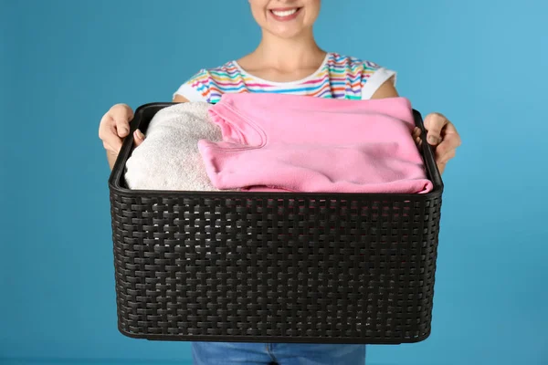 Mujer joven sosteniendo cesta con ropa sobre fondo de color, primer plano — Foto de Stock