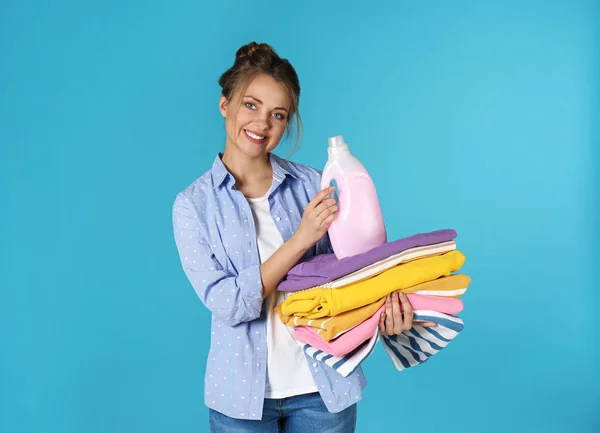Happy young woman holding clean clothes and laundry detergent on color background — Stock Photo, Image