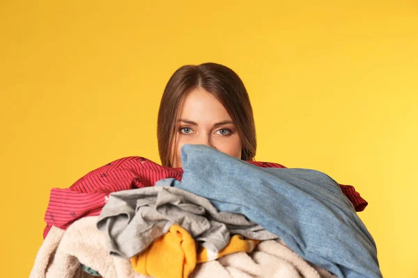 Mujer joven sosteniendo pila de ropa sucia en el fondo de color — Foto de Stock