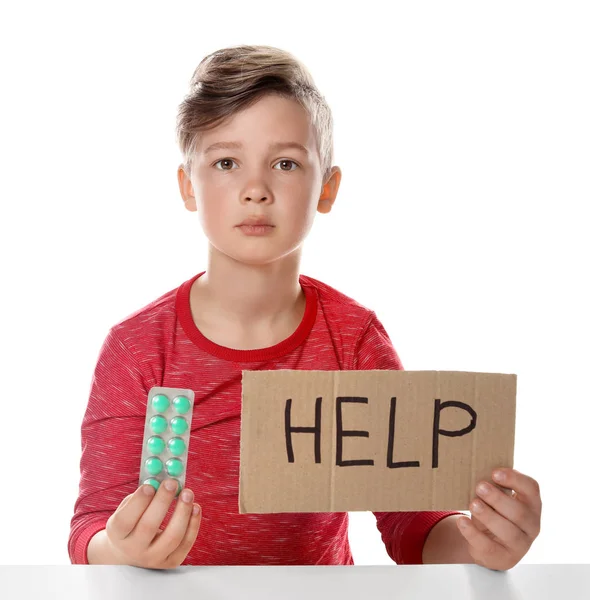 Niño pequeño con pastillas y palabra Ayuda escrita en cartón sobre fondo blanco. Peligro de intoxicación por medicamentos — Foto de Stock