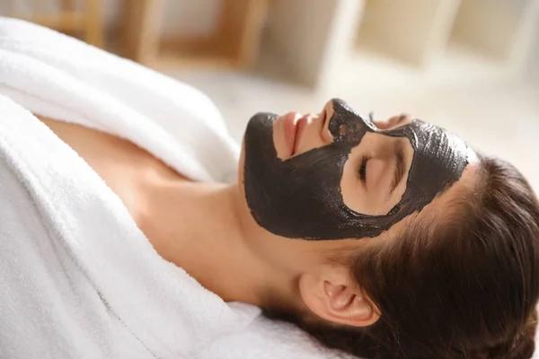 Belle femme avec masque noir sur le visage relaxant dans le salon de spa — Photo
