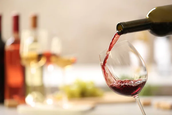 Verter el vino tinto de la botella en un vaso sobre un fondo borroso. Espacio para texto — Foto de Stock
