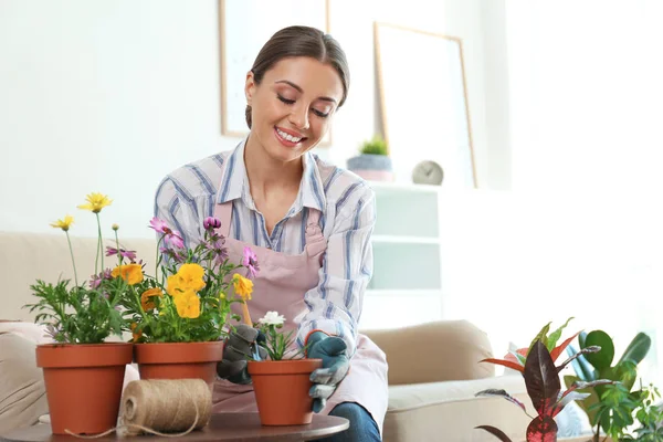 Mujer joven cuidando plantas en maceta en casa — Foto de Stock