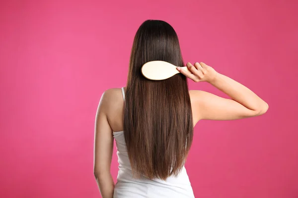 Visão traseira da jovem com escova de cabelo no fundo de cor — Fotografia de Stock