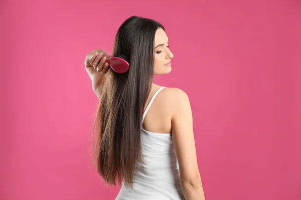 Beautiful young woman with hair brush on color background — Stock Photo, Image