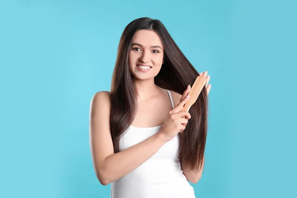Bela jovem sorridente com escova de cabelo no fundo de cor — Fotografia de Stock