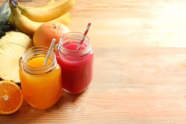 Diferentes jugos en tarros de albañil y frutas frescas en mesa de madera. Espacio para texto — Foto de Stock