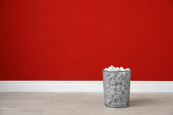 Metal bin with crumpled paper on floor against color wall. Space for text